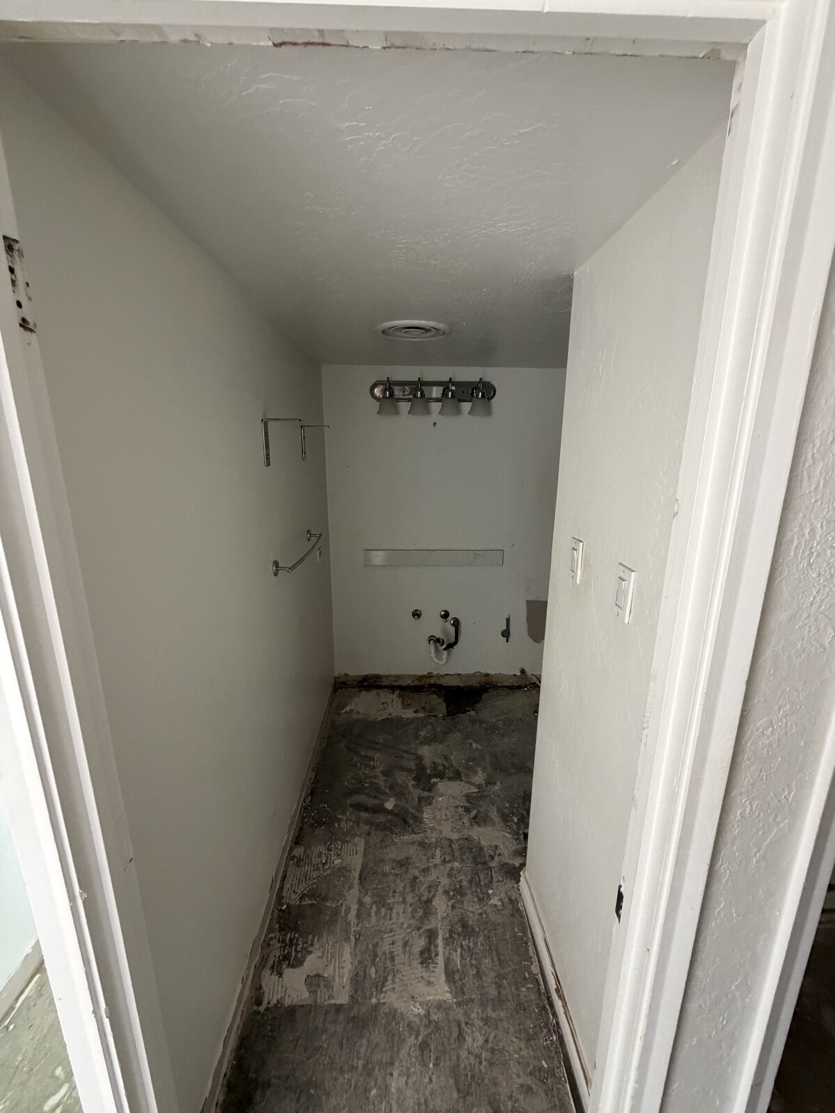 Laundry closet with flooring and appliances removed, leaving bare subfloor and capped water lines