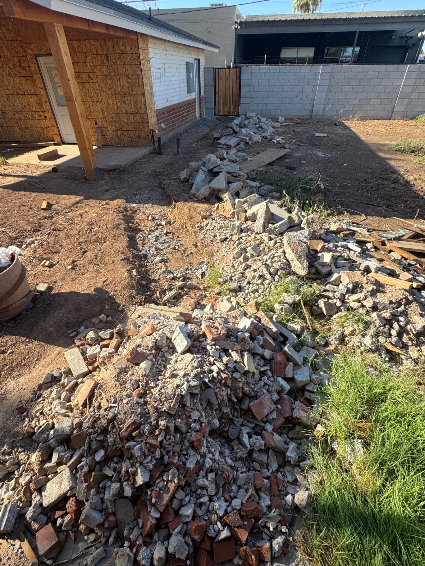 Backyard with broken concrete, brick, and lumber debris piled up alongside a home addition, staged for haul-off