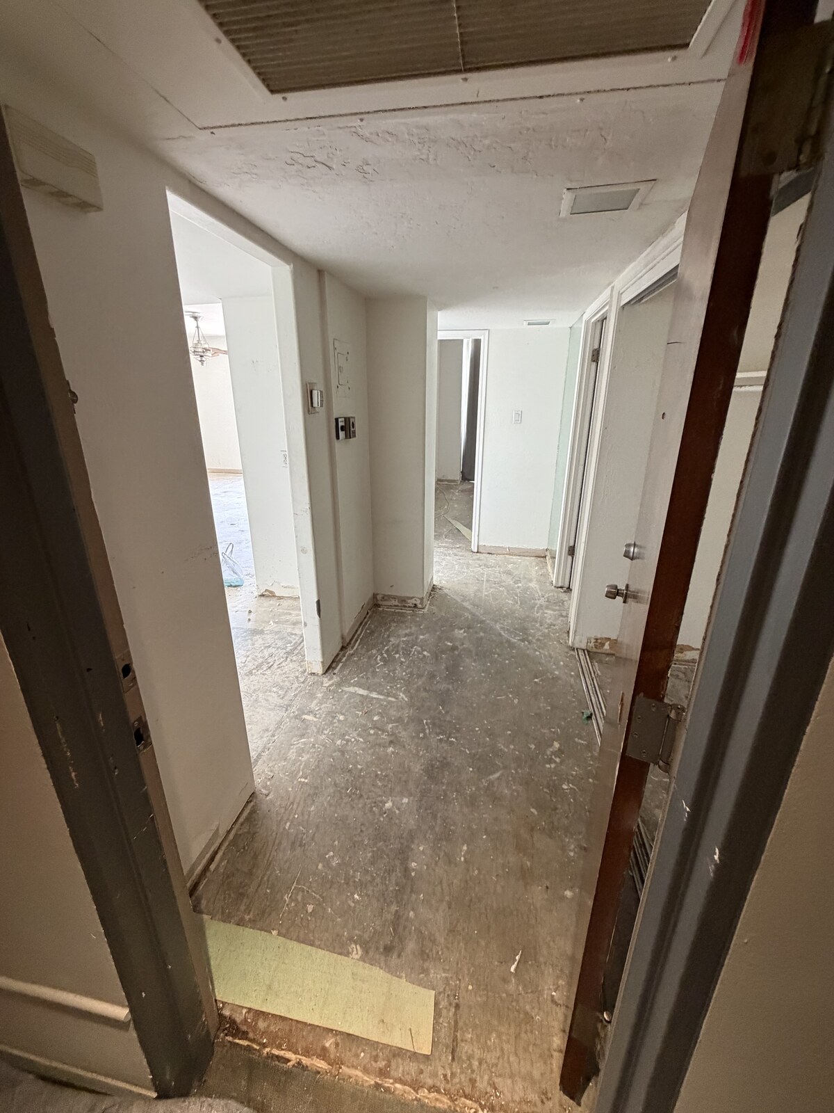 Hallway and adjoining rooms stripped of carpet and baseboards down to bare subfloor